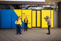 Tre personer i gula och blå IKEA-uniformer står framför en butik när en fotograf tar bilder.