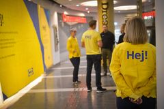 Personer i gula jackor med texten "Hej!" står och pratar i en butiksgalleria.