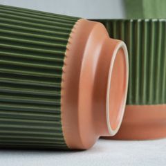 Två keramikvaser med räfflad grön yta och orange botten placerade på sidan.