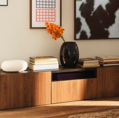 Bokhylla i trä med böcker, en vit lampa och en svart vas med orange blommor.