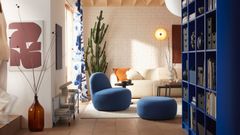 Ett modernt vardagsrum med blå fåtölj och fotpall, beige soffa, stor kaktus och blå bokhylla.