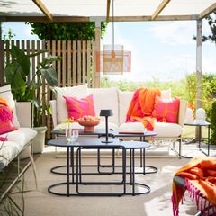 Alt-text: Utomhus vardagsrum med vita soffor, färgglada kuddar och filtar, och moderna svarta soffbord.