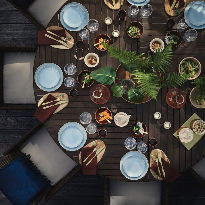 En%20rund%20borddukning%20ovanifr%E5n%20med%20tallrikar%2C%20glas%20och%20sk%E5lar%2C%20dekorerad%20med%20gr%F6na%20v%E4xter.