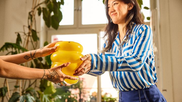 En person räcker över en gul vas till en annan person.