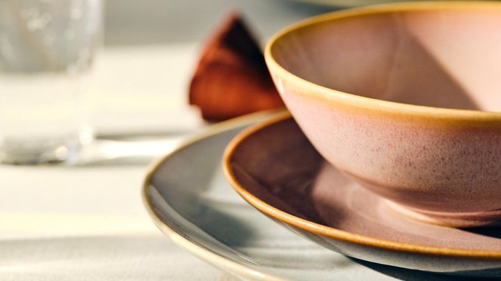 På ett vitt bord syns en dukning med en grå tallrik, en rosa tallrik och en rosa skål.