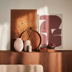 Alt-text: Dekorativt arrangemang med abstrakt konstverk, vaser och träring på en hylla.