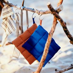 Grytlappar i brunt och blått hänger från en gren på en strand.