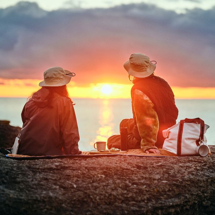 Tv%E5%20personer%20sitter%20p%E5%20en%20klippa%20och%20tittar%20p%E5%20en%20solnedg%E5ng%20%F6ver%20havet.
