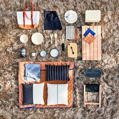 Överblick av picknickutrustning arrangerad på marken, inklusive tallrikar, bestick, en grill och kuddar.