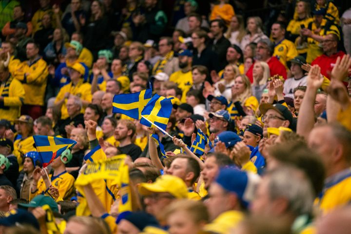 En folkmassa iklädd gula och blå kläder, viftande med svenska flaggor vid ett evenemang.