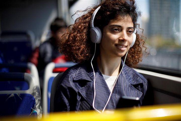 Kvinna med hörlurar sitter och lyssnar på musik på en buss.