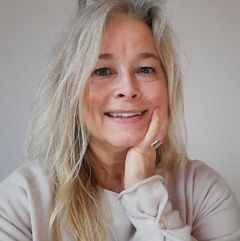 En kvinna, Liise Dahlqvist, med långt ljust hår ler mot kameran. Hon bär en ljus tröja och stöder sitt ansikte med handen.