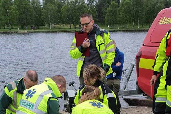 Grupp ambulanssjukvårdare övar vid vattnet bredvid en räddningsbil.