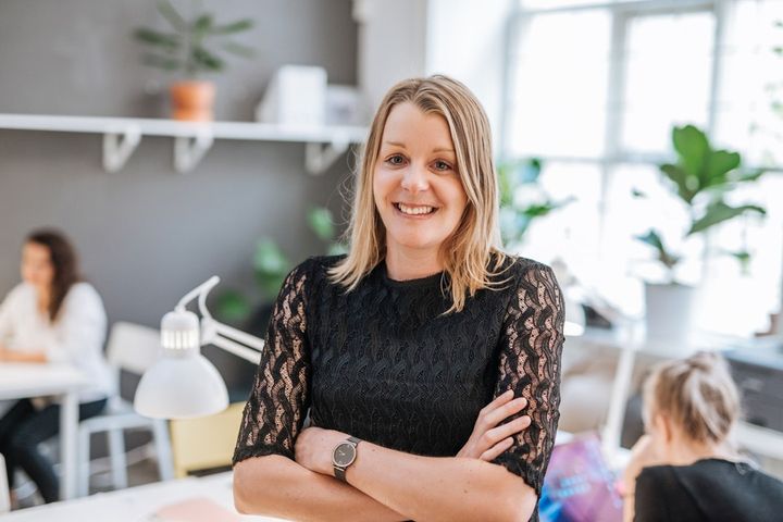 En leende person står med armarna i kors i ett ljust kontor.