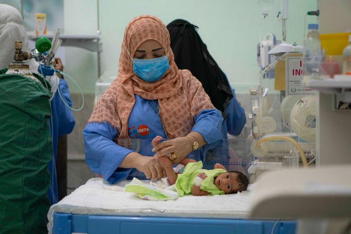 En kvinna i blå uniform byter blöja på ett barn i ett sjukhusrum.