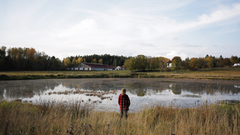 En lantbrukare står framför en vattenfylld bevattningsdamm intill åkermark.