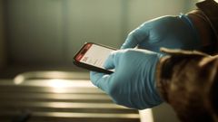 En jägare har tagit på sig engångshandskar och hanterar en mobil med SVA:s app Trikintest.