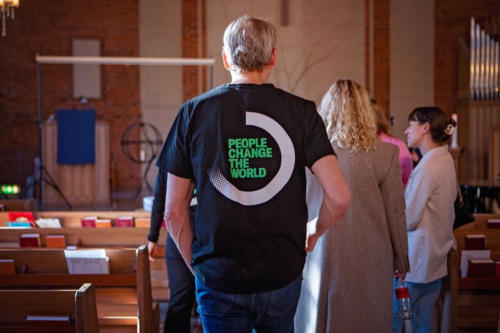 Människor i en kyrka. Texten People change the world på en t-shirt.