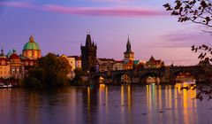 Utsikt över Karlsbron och floden i Prag i skymningen med upplysta byggnader.