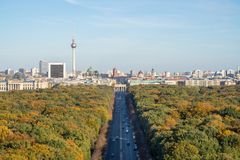 Utsikt över Berlin med TV-tornet i fjärran och en väg omgiven av träd i höstfärger.