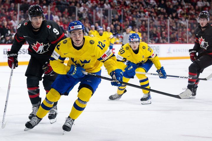 Ishockeyspelare från Sverige och Kanada tävlar om pucken på isen under en match.