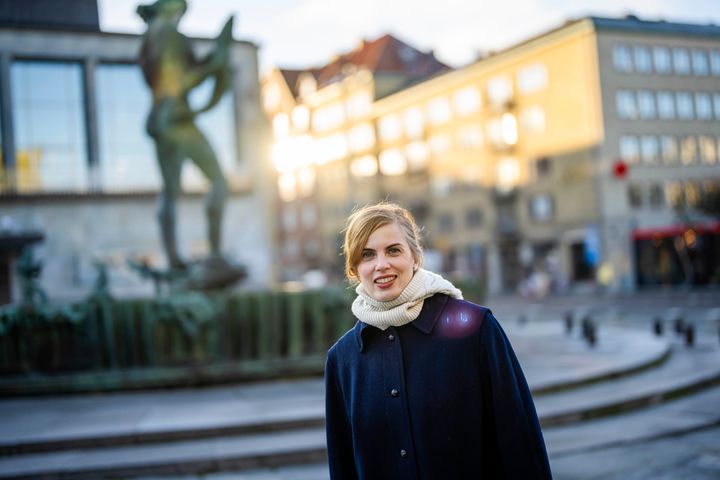 Författaren Lydia Sandgren står på Götaplatsen framför en fontän och byggnader i en stadsmiljö.