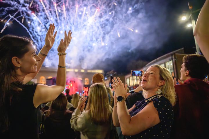 Publik på en utomhus konsert med fyrverkeri i bakgrunden.