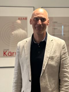 En person med en ljus kavaj står framför en vägg med inramade dokument.