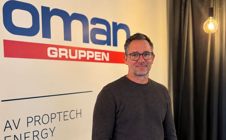Man med glasögon står framför en skylt med Ömangruppen på. Ijämte honom en lampa.