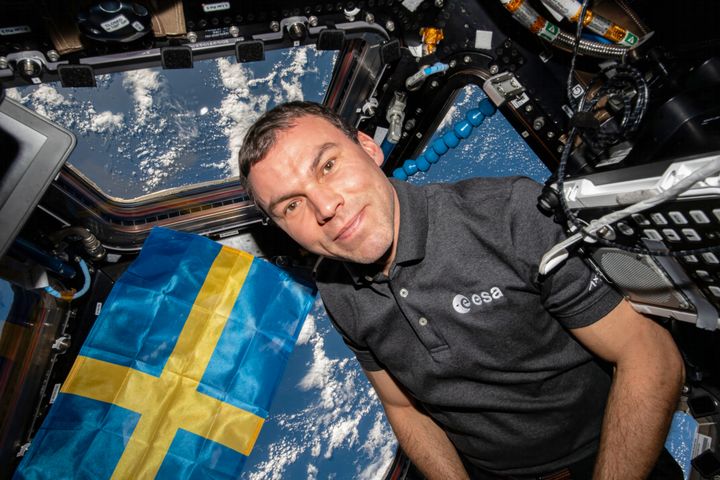 Bild av Marcus Wandt i en rymdkapsel med en svensk flagga i bakgrunden.