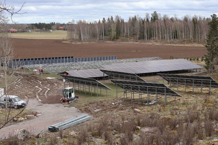 Övergripande bild på hela solcellsparken med de olika typerna av paneler, och en gård längre bort i bakgrunden