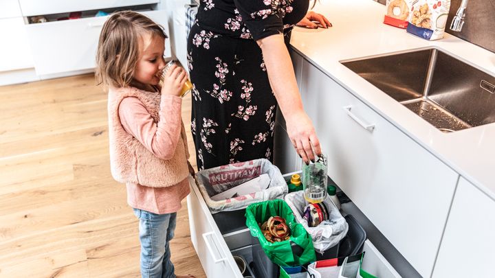 Kvinna med barn som slänger skräp i ett fack i en låda med återvinningskärl