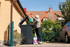 Kvinna i helfigur står vid en sorteringstunna där hon lägger en grön påse