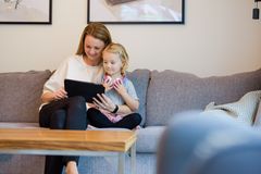 Kvinnlig förälder med barn sitter i en soffa och tittar på en i-pad, varm och mysig stämning