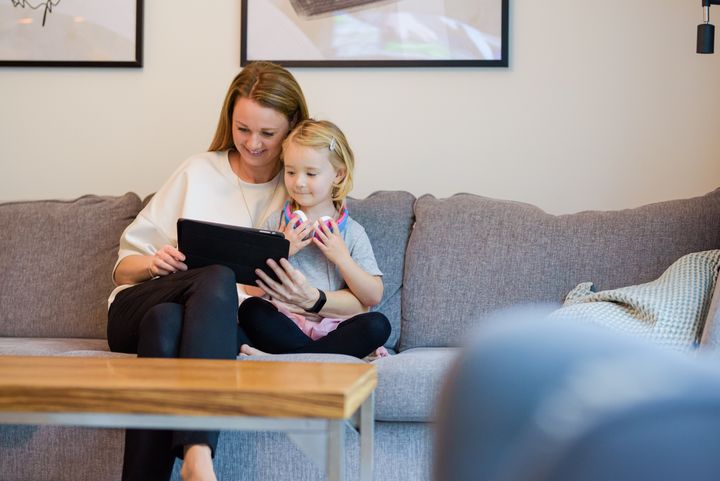 Kvinnlig förälder med barn sitter i en soffa och tittar på en i-pad, varm och mysig stämning