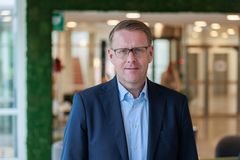 Medelålders man i halvfigur med glasögon och gråkaval, som tittar in i kameran, något leende