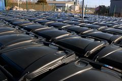 Stora mängder svarta avfallskärl står uppställda tätt i rader på ett inhägnat område utomhus vid en industrilokal.