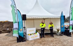 En man och kvinna i gula varseljackor står tillsammans framför ett vitt tält med varsin mikrofon i handen och talar inför spadtaget