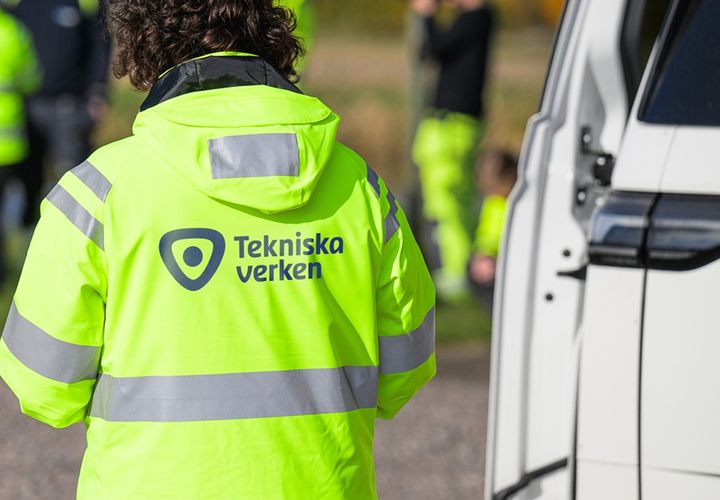 Medarbetare i halvfigur står med ryggen mot kameran bredvid en vit skåpbil, med gul varseljacka som har logotypen Tekniska verken.
