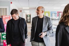 Två personer i affärsmiljö går tillsammans i en ljus kontorskorridor, klädda i kavaj och mörka kläder, med fokus på dialog och samarbete.