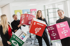Fyra personer håller upp stora kuber med symboler för globala hållbarhetsmål.