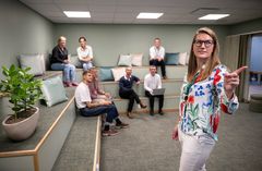 Ett atrium med en gradäng där sju personer tittar på en kvinna i bildens framkant som pekar mot en skärm utanför bilden.