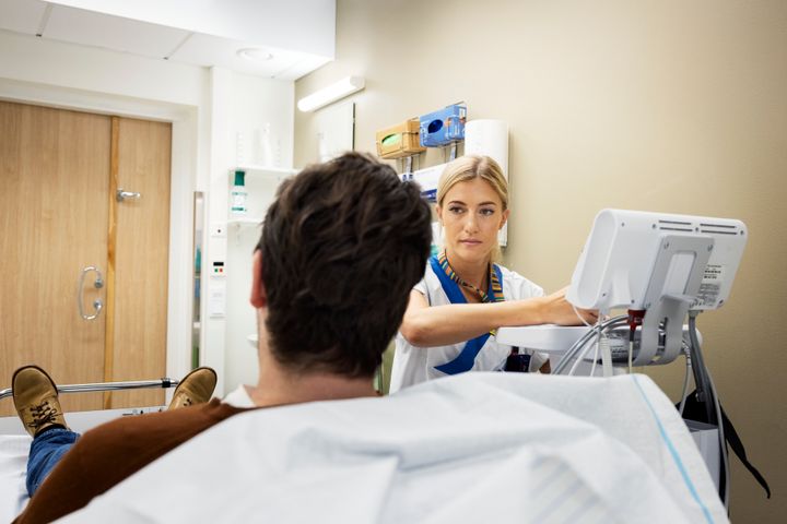 En kvinnlig sjuksköterska sitter samtalar med en patient och skriver i en dator.