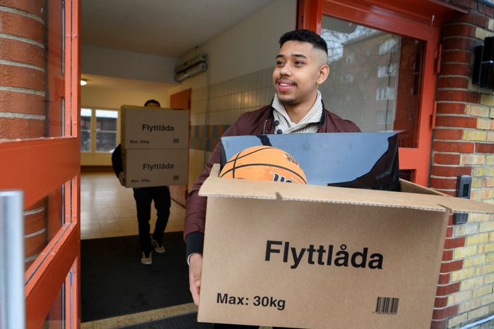 Två personer bär flyttlådor ut ur en byggnad.