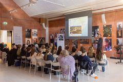 En grupp människor lyssnar på en presentation i ett galleri. En person visar bilder på en projektorduk.
