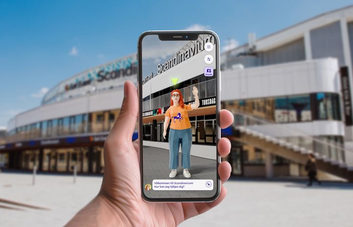 En digital bild, där en avatar hälsar dig välkommen via telefonen. I bakgrunden ser du Scandinavium.