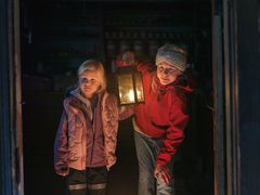 Två barn lyser med en lykta i en av Skansens historiska miljöer.