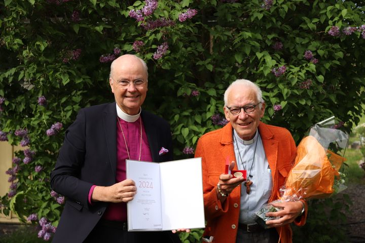 Biskop Johan Dalman och Knut Fischer framför syrenbuske. De uppvisar diplom, blommor och Strängnäs stifts förtjänsttecken.på Stiftsgården Stjärnholm.