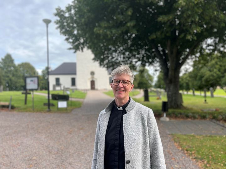 Kvinna i prästkläder som står utomhus framför en kyrka.
