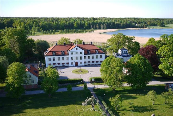 Flygfoto av Stiftsgården Stjärnholm omgiven av grönska och en sjö i bakgrunden.